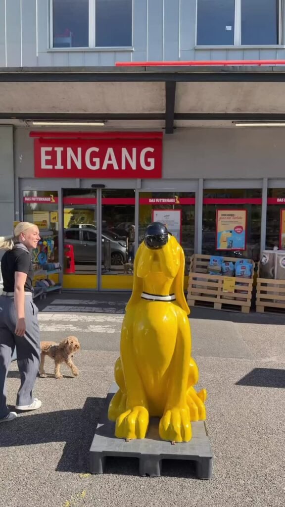 Mareike mit ihrem Hund Tuula vor dem Eingang einer Futterhaus-Filiale, daneben eine gelbe Hundefigur