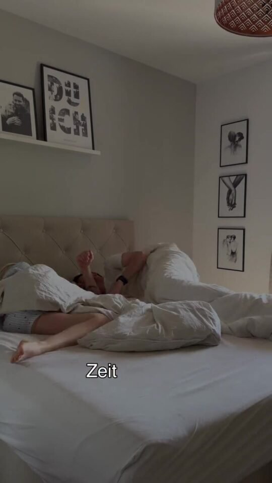 Zwei Personen liegen morgens unter einer Bettdecke in einem Schlafzimmer