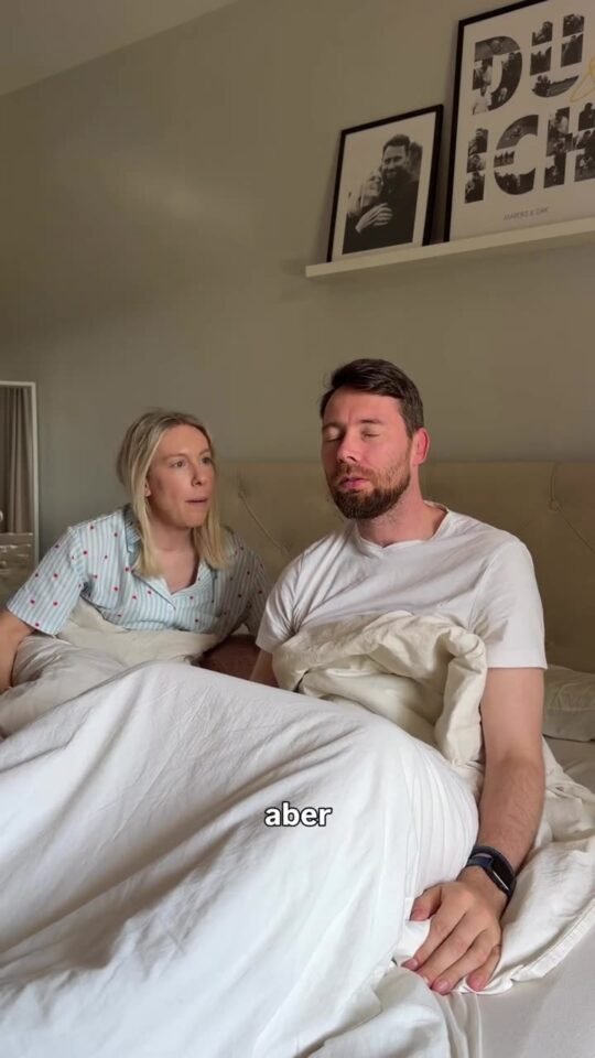 Mareike und ihr Partner sitzen morgens im Bett unter einer weißen Decke