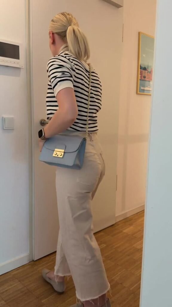 Mareike in gestreiftem Shirt mit hellblauer Umhängetasche an einer Wohnungstür