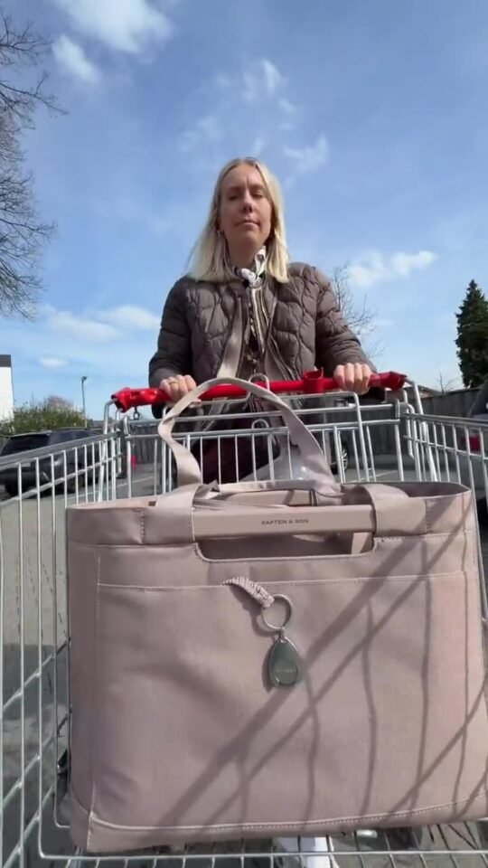 Mareike schiebt einen Einkaufswagen mit einer rosafarbenen Tasche von Kapten & Son an einem sonnigen Tag